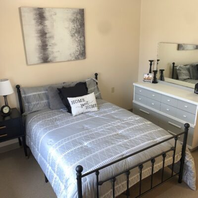 A neatly made bed with a black metal frame, gray and white bedding, and a decorative pillow that says 